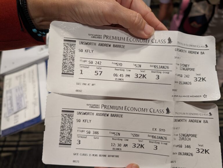 Two Singapore Airlines Premium Economy boarding passes — SQ242 Sydney to Singapore and SQ346 Singapore to Zurich — held in hand at Sydney Airport, January 2026