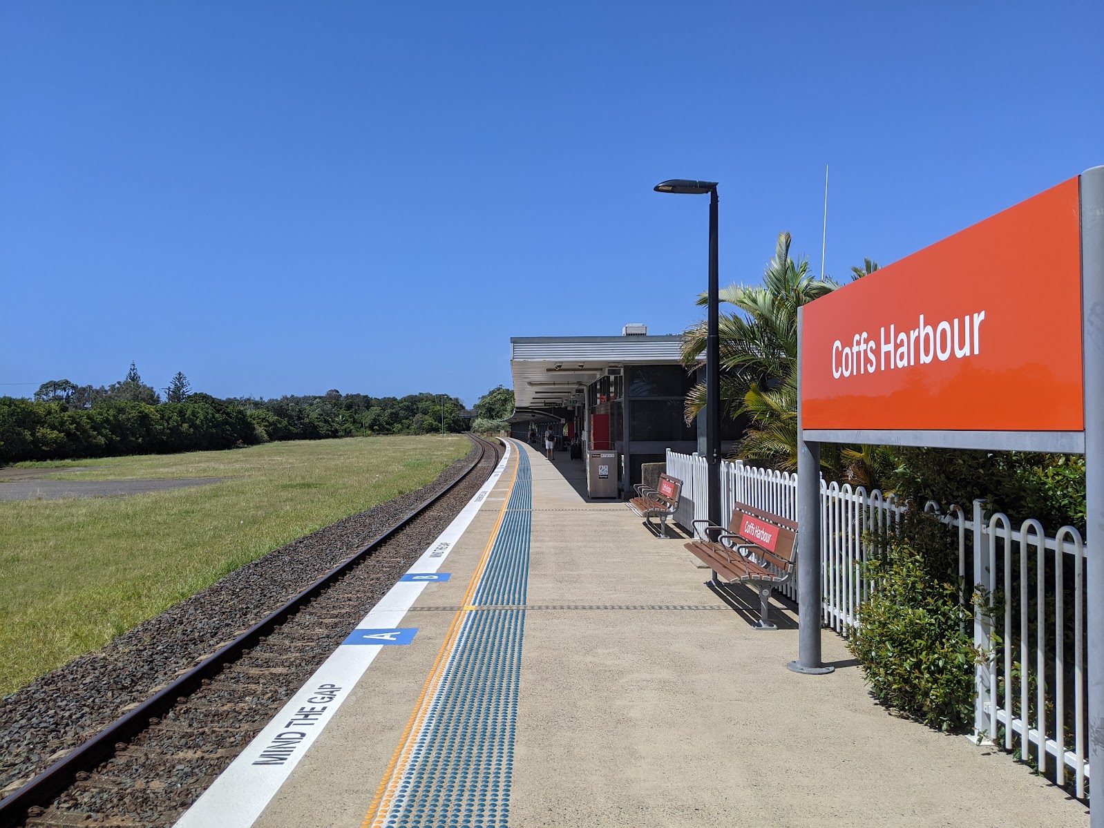 Coffs Harbour railway station platform in the sun with the orange NSW TrainLink sign and palm trees