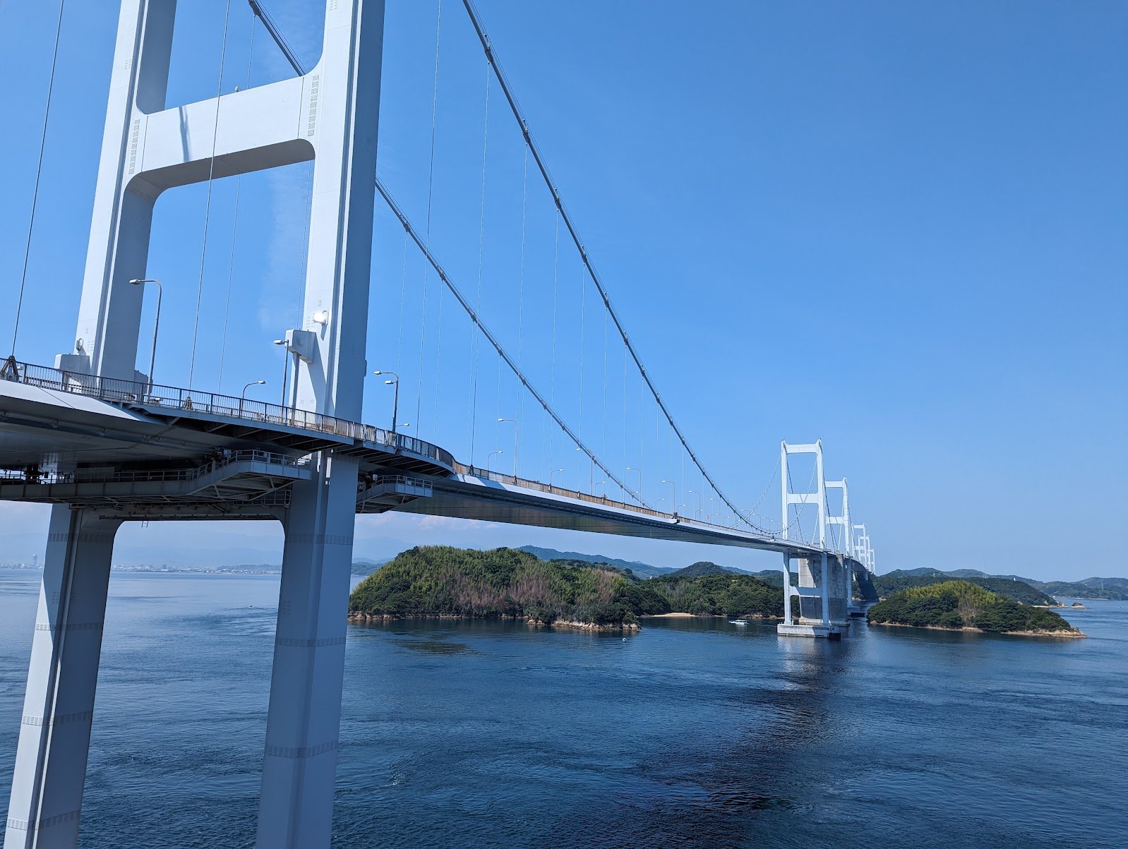 The Kurushima Kaikyo Bridge stretching across the Seto Inland Sea over green islands, seen from the cycle path on the approach to Imabari — June 2024