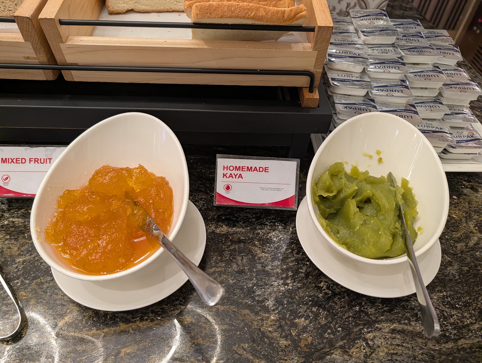 Two white bowls of homemade kaya jam on a buffet counter at SATS Premier Lounge Changi, with Lurpak butter and toast behind