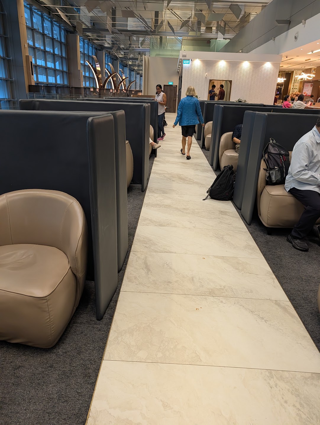 Aisle between high-backed partitioned seating pods at SATS Premier Lounge Terminal 3, with floor-to-ceiling windows on the left