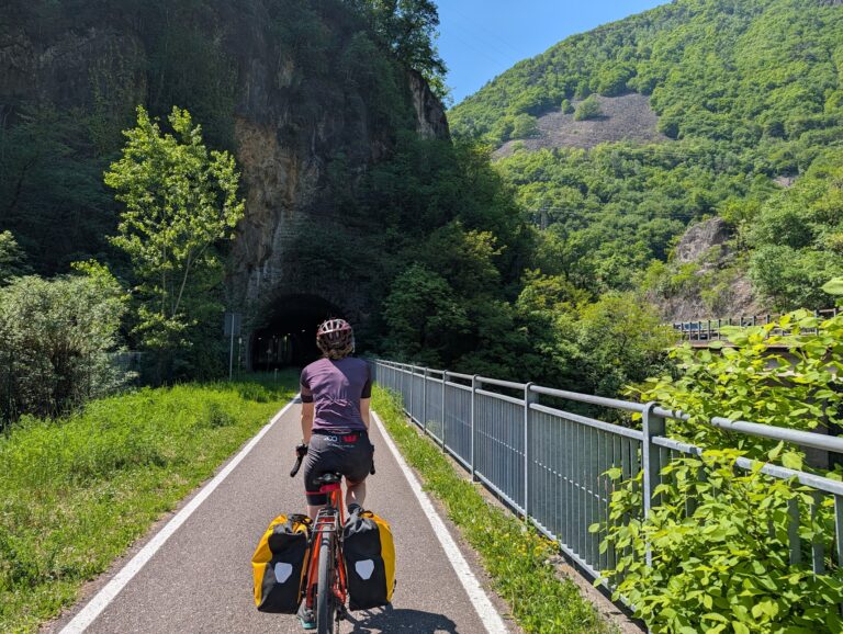 Cyclist on EuroVelo 7 approaching an alpine tunnel, fully loaded panniers, northern Italy, April 2026