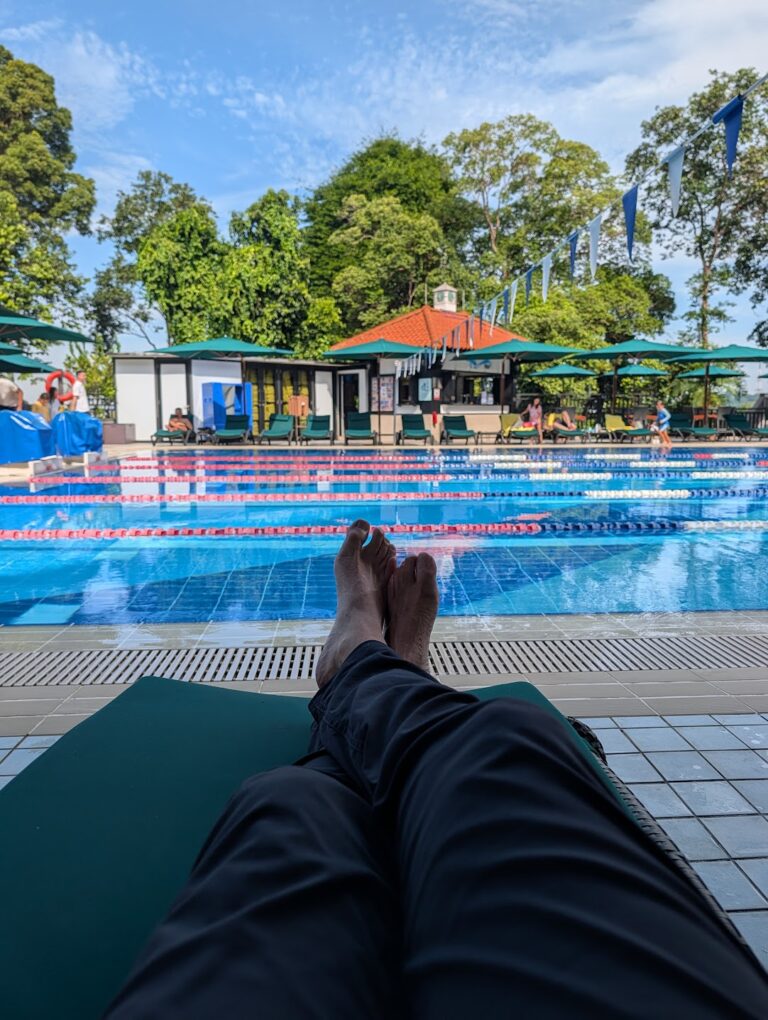 The British Club pool and arched clubhouse, Singapore, seen from a poolside lounger