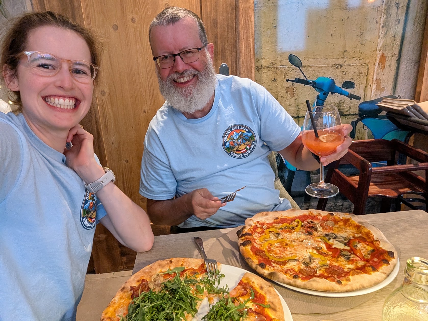Gravel Alps 2026 matching t-shirts worn over pizza in Italy