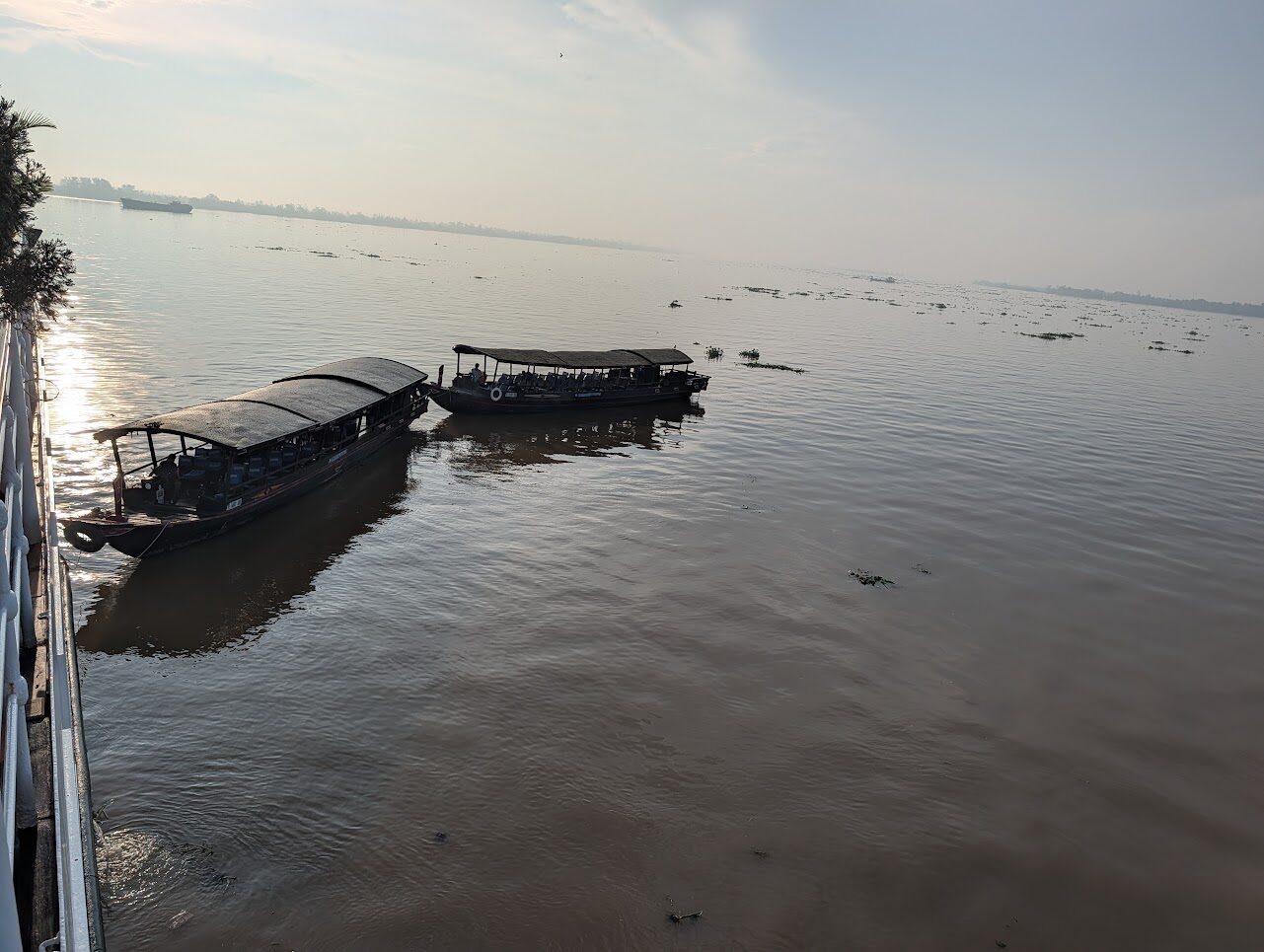 Two excursion boats waiting alongside La Marguerite on the Mekong at sunrise