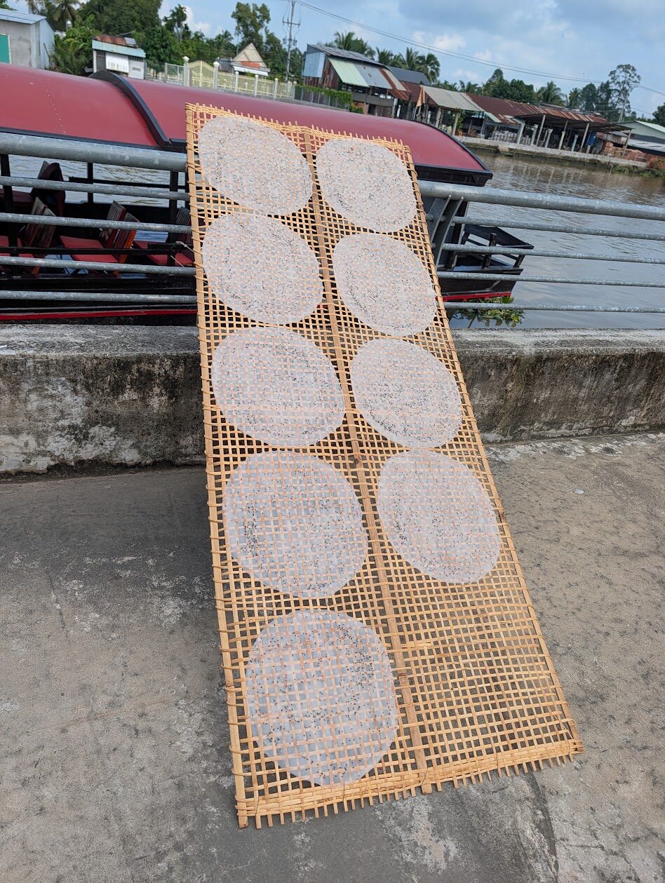 Rice paper rounds drying on a bamboo rack beside a Mekong Delta canal
